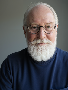 A portrait of a senior man with balding gray hair and a full white beard